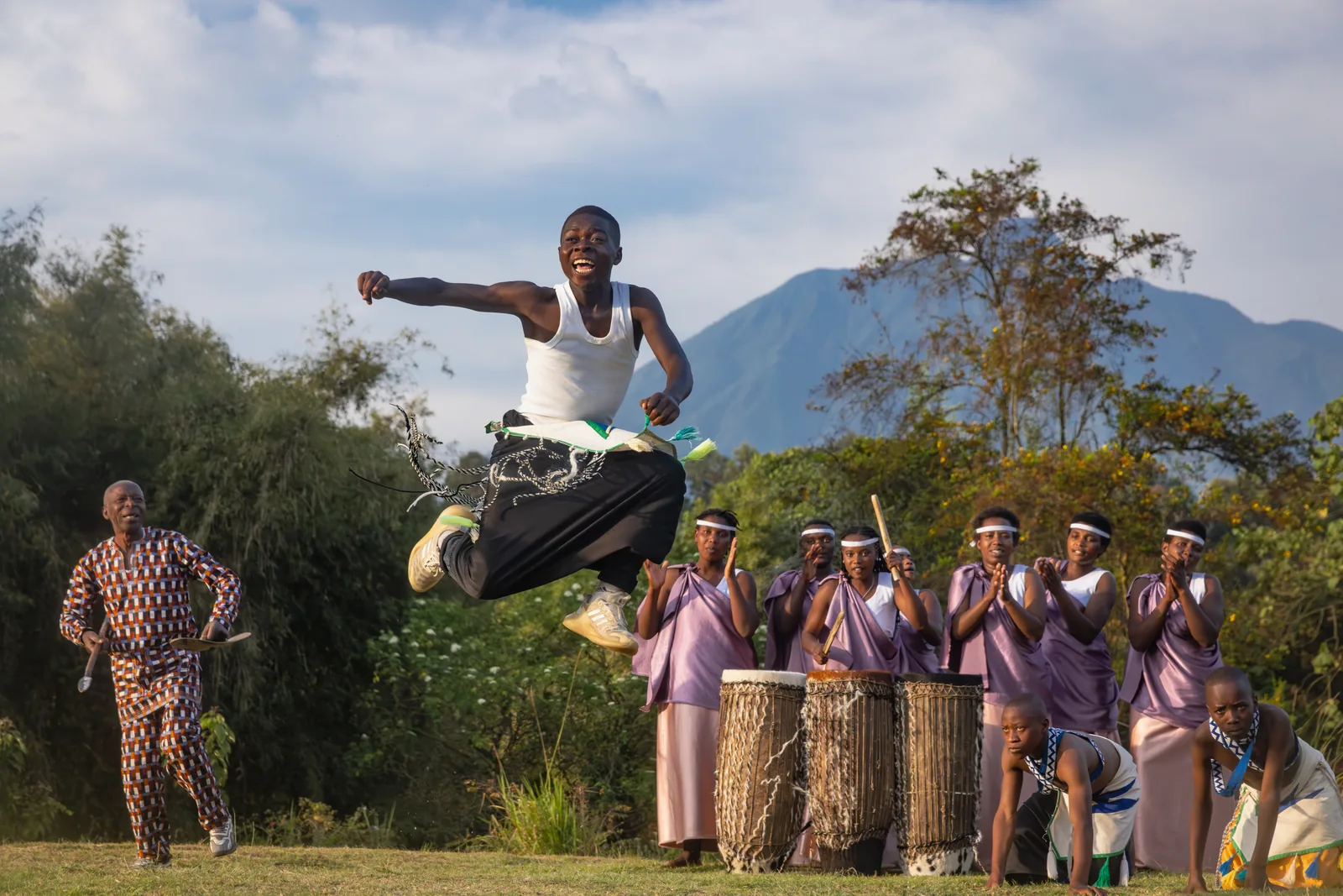 Intore dancer leaping mid-air while drummers and dancers perform